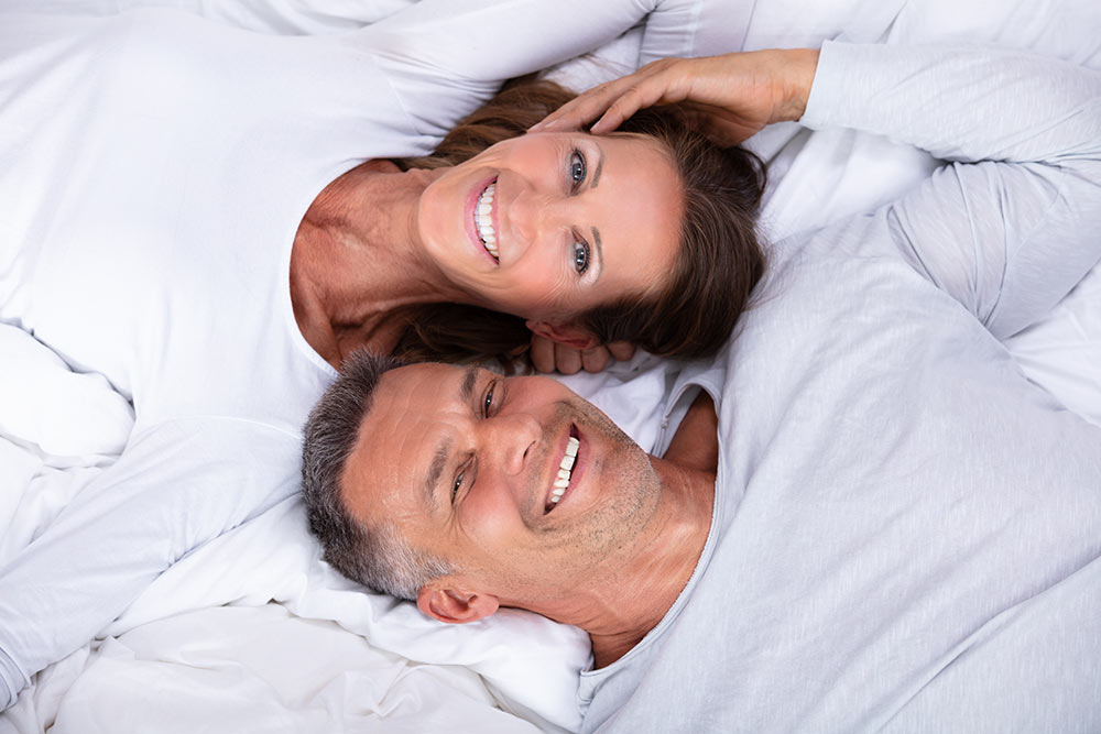 A couple in bed smiling | West Charlotte Dental Services